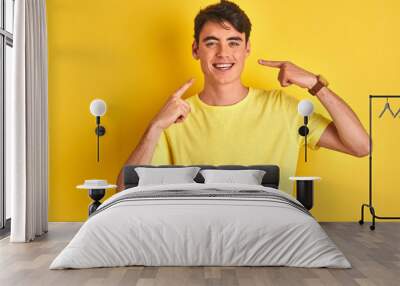 teenager boy wearing yellow t-shirt over isolated background smiling cheerful showing and pointing w Wall mural