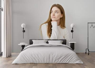 Thoughtful young caucasian woman in casual attire posing against a white background, embodying beauty and youth. Wall mural