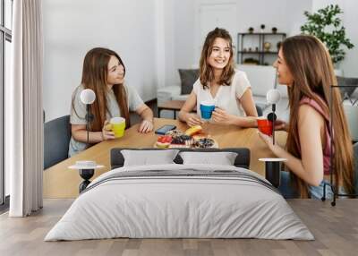 Three young friends woman smiling happy having breakfast sitting on the table at home. Wall mural