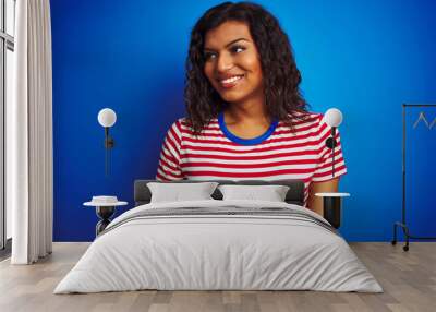 Transsexual transgender woman wearing stiped t-shirt over isolated blue background looking away to side with smile on face, natural expression. Laughing confident. Wall mural