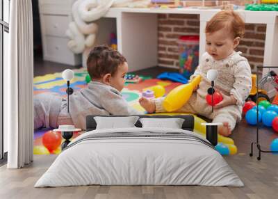 Two adorable babies playing with balls and bowling pin sitting on floor at kindergarten Wall mural