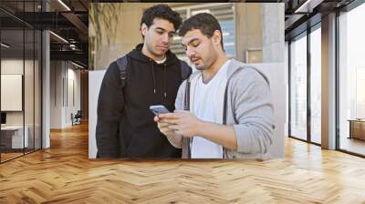 Two hispanic men using a smartphone together on a city street. Wall mural