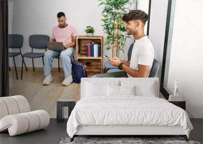 Two hispanic men using laptop and smartphone sitting on chair at waiting room Wall mural