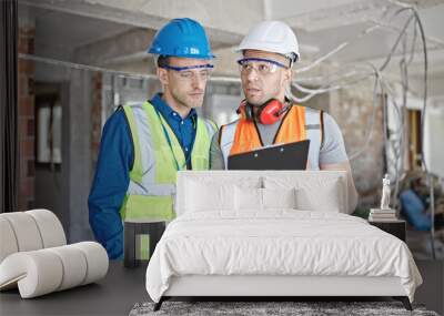 Two men builders reading document speaking at construction site Wall mural