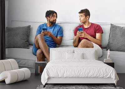 Two men friends using smartphone sitting on sofa at home Wall mural