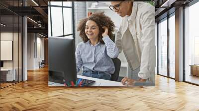 Two team partners, a man and a woman, enjoy working together at the office, smiling confidently while using a computer in indoor professional surroundings Wall mural