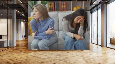 Two women, friends or sisters, appear sad and thoughtful in a cozy living room Wall mural