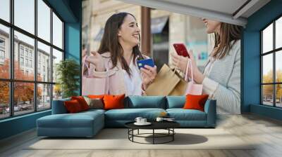 Two women going shopping using smartphone and credit card at street Wall mural