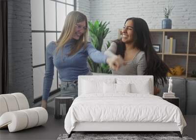 Two women laughing and dancing together in a modern living room with a cozy sofa and stylish decor Wall mural