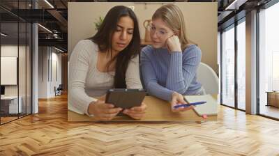 Two women studying together in a modern apartment, sharing a tablet and taking notes Wall mural