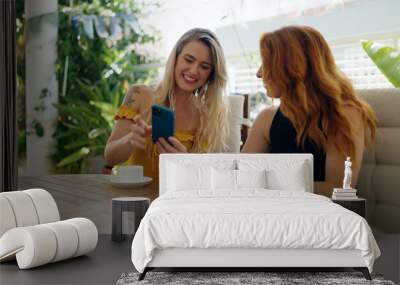 Two women using smartphone and drinking coffee sitting on table at home terrace Wall mural