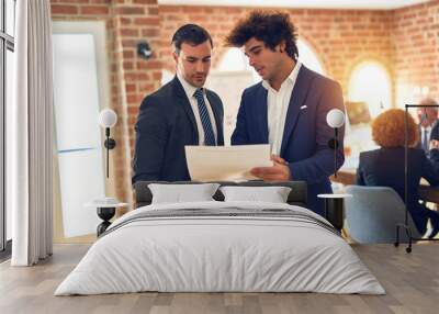 Two young handsome businessmen working together. Speaking and reading documents standing at the office Wall mural