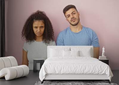 Unhappy couple standing against a plain pink wall showcasing relationship issues. Wall mural