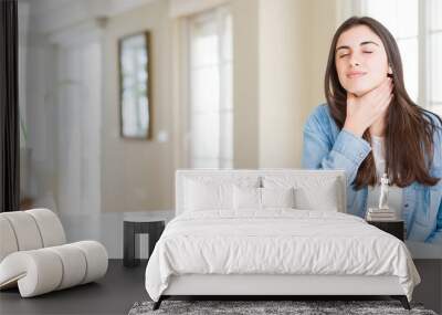 Wide angle picture of beautiful young woman sitting on white table at home Touching painful neck, sore throat for flu, clod and infection Wall mural