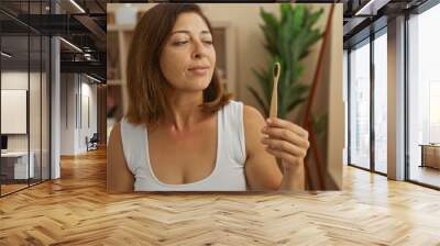 Woman holding toothbrush in spa room with wellness products and plants, capturing serene and beautiful setting of middle-aged brunette enjoying indoor beauty treatment Wall mural