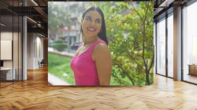 Woman wearing pink top smiling in an urban park with greenery and city buildings in the background on a sunny day Wall mural