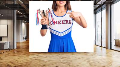 Youn beautiful asian girl wearing cheerleader uniform holding champion trophy smiling happy pointing with hand and finger Wall mural