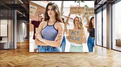 Young activist woman with arms crossed gesture standing with a group of protesters holding banner protesting at the city. Wall mural