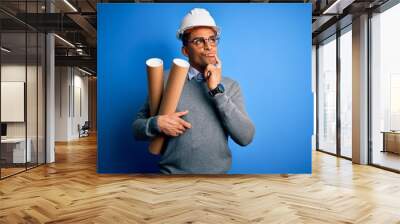 Young african american afro architect man wearing safety helmet holding bluprints serious face thinking about question, very confused idea Wall mural