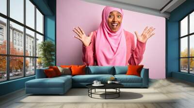 Young African American afro woman wearing muslim hijab over isolated pink background celebrating crazy and amazed for success with arms raised and open eyes screaming excited. Winner concept Wall mural