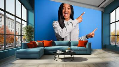 Young african american athlete woman wearing sports sweatshirt over blue isolated background smiling and looking at the camera pointing with two hands and fingers to the side. Wall mural