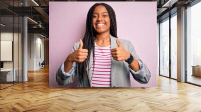 Young african american business woman standing over pink isolated background success sign doing positive gesture with hand, thumbs up smiling and happy. Cheerful expression and winner gesture. Wall mural