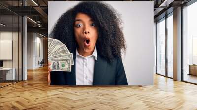 Young african american business woman with afro hair holding cash dollars banknotes scared in shock with a surprise face, afraid and excited with fear expression Wall mural