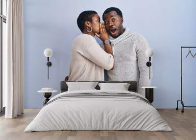 Young african american couple standing over blue background together hand on mouth telling secret rumor, whispering malicious talk conversation Wall mural