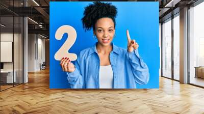 Young african american girl holding number two smiling with an idea or question pointing finger with happy face, number one Wall mural