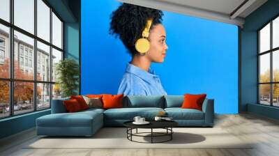 Young african american girl listening to music using headphones looking to side, relax profile pose with natural face with confident smile. Wall mural