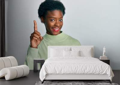 Young african american girl wearing casual clothes showing and pointing up with finger number one while smiling confident and happy. Wall mural