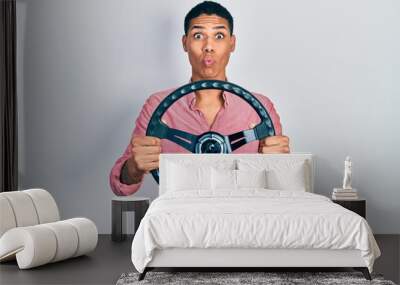 Young african american guy holding steering wheel making fish face with mouth and squinting eyes, crazy and comical. Wall mural