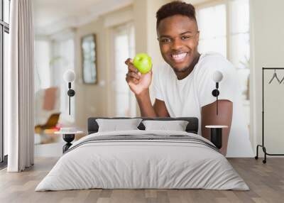 Young african american man eating fresh green apple with a happy face standing and smiling with a confident smile showing teeth Wall mural