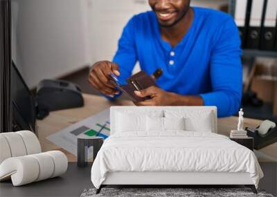 Young african american man ecommerce business worker holding wallet with credit card at office Wall mural