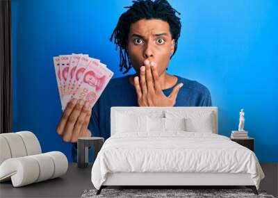 Young african american man holding 10 yuan chinese banknotes covering mouth with hand, shocked and afraid for mistake. surprised expression Wall mural