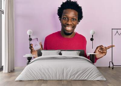 Young african american man holding engagement ring for proposal smiling happy pointing with hand and finger to the side Wall mural