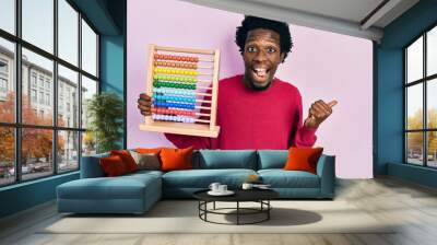 Young african american man holding traditional abacus pointing thumb up to the side smiling happy with open mouth Wall mural