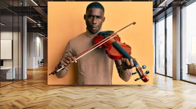 Young african american man playing violin making fish face with mouth and squinting eyes, crazy and comical. Wall mural