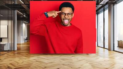 Young african american man pointing head with finger sticking tongue out happy with funny expression. Wall mural