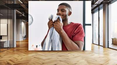 Young african american man smiling confident smelling clean clothes at laundry room Wall mural