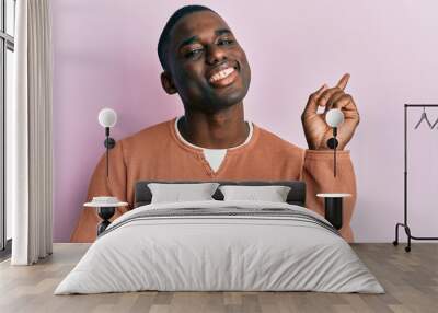 Young african american man wearing casual clothes with a big smile on face, pointing with hand and finger to the side looking at the camera. Wall mural