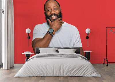 Young african american man wearing casual white tshirt looking confident at the camera smiling with crossed arms and hand raised on chin. thinking positive. Wall mural