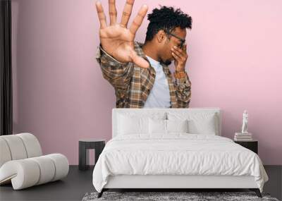 Young african american man with beard wearing casual clothes and glasses covering eyes with hands and doing stop gesture with sad and fear expression. embarrassed and negative concept. Wall mural