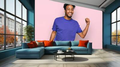 Young african american man with beard wearing casual purple t shirt smiling with happy face looking and pointing to the side with thumb up. Wall mural