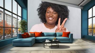 Young african american plus size woman over grey grunge wall wearing winter sweater smiling with happy face winking at the camera doing victory sign. Number two. Wall mural