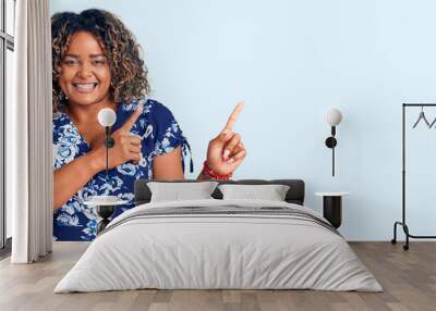 Young african american plus size woman wearing casual clothes smiling and looking at the camera pointing with two hands and fingers to the side. Wall mural