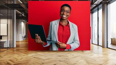 Young african american woman holding laptop looking positive and happy standing and smiling with a confident smile showing teeth Wall mural