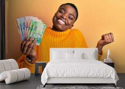 Young african american woman holding south african rand banknotes screaming proud, celebrating victory and success very excited with raised arm Wall mural