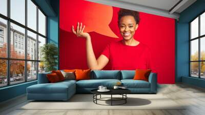 Young african american woman holding speech bubble over red isolated background with a happy face standing and smiling with a confident smile showing teeth Wall mural