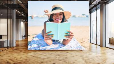 Young african american woman on vacation laying on the towel reading book at the beach Wall mural